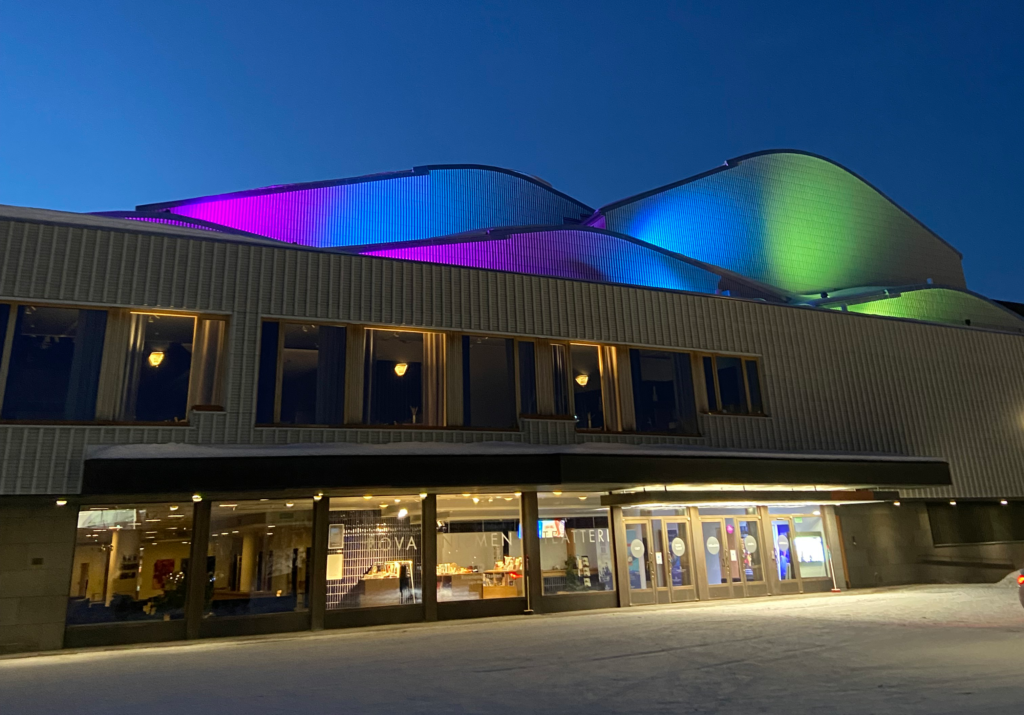Kuvassa Rovaniemen teatteri illalla, aaltomuodot katolla on valaistu värikkäästi pinkillä, sinisellä ja vaalean vihreällä.