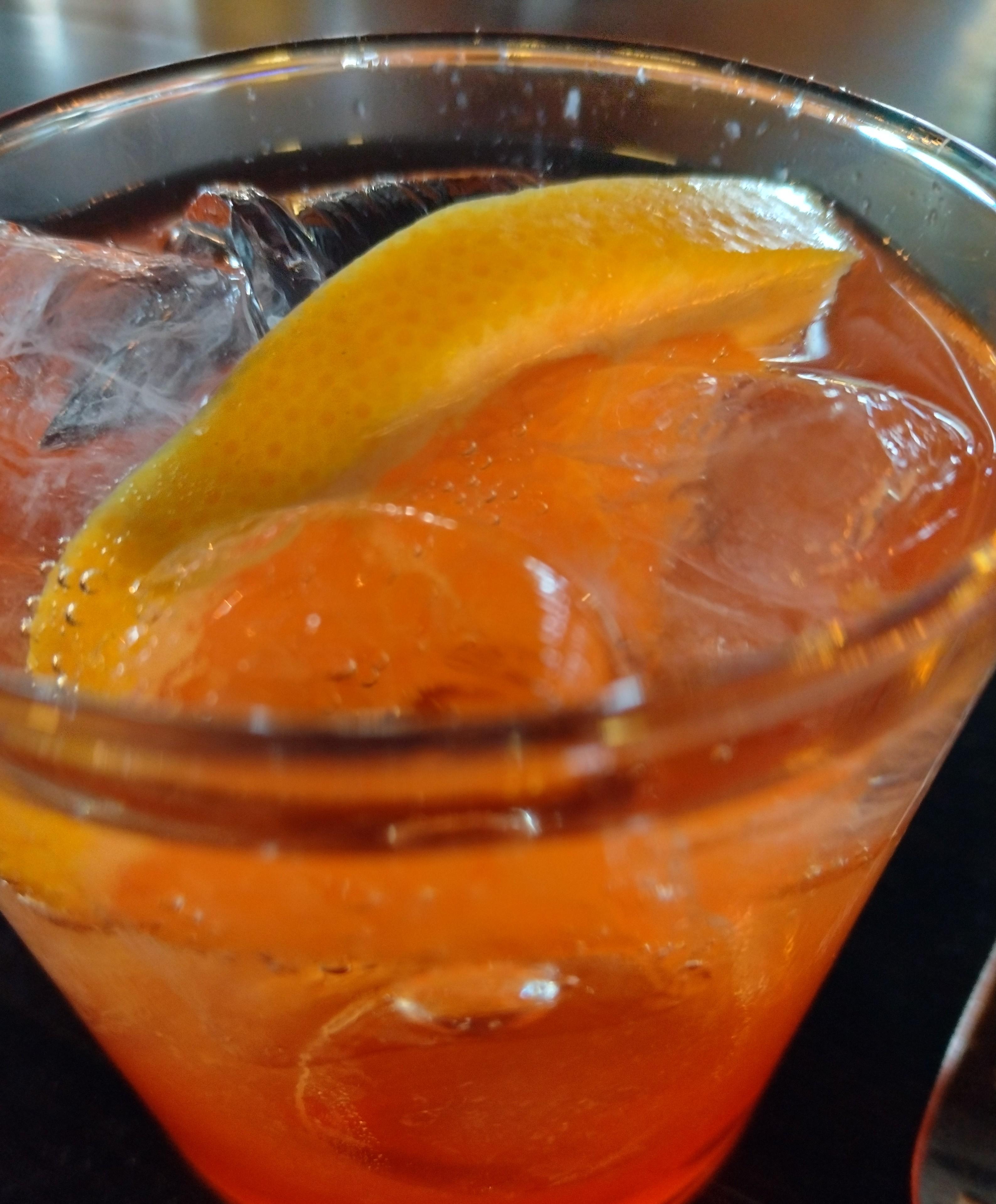 Kuvassa oranssin värinen drinkki lähikuvassa, lasissa on myös jäitä.