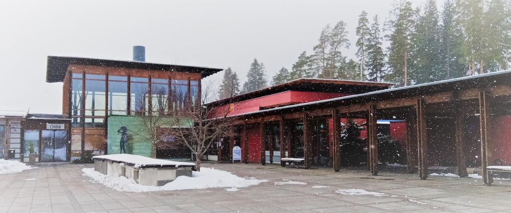 Hyvinvointikeskus Onnin punainen rakennus kevyessä lumisateessa. Maa on miltei lumeton.