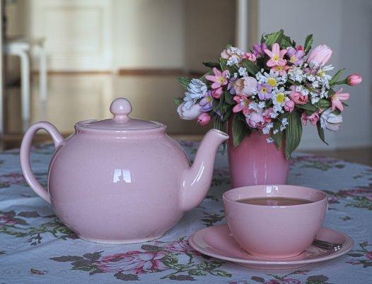 Kuvituskuva, jossa pöydällä kukkakimppu sekä vaaleanpunainen teekannu ja kuppi
