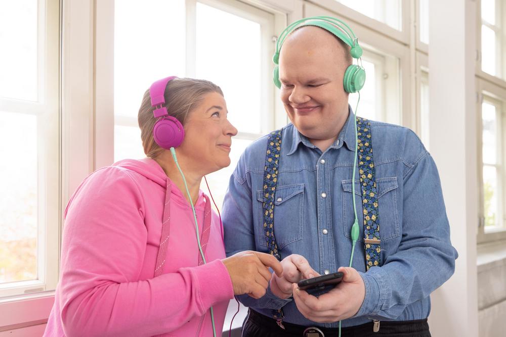 Kaksi henkilö kuuntelee kuulokkeilla äänikirjaa älypuhelimesta