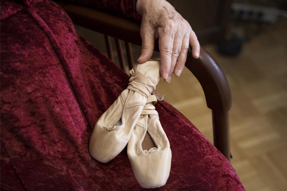 punamekkoisen vanhan naisen kädessä on kuluneet balettitossut