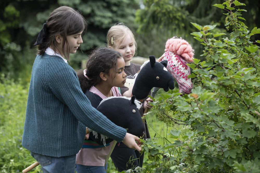 Kolme laste keppihevosten kanssa leikkimässä