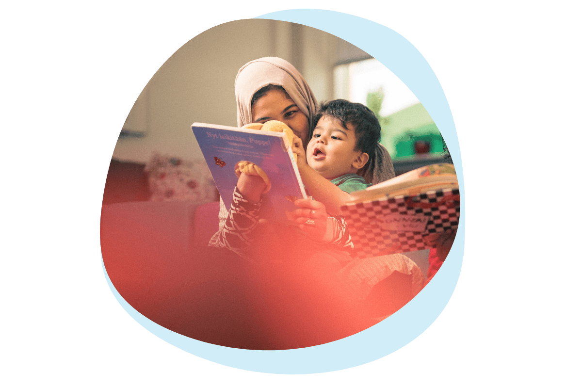 Maahan muuttanut äiti lukee lapselle kirjaa ja lapsi hymyilee Koivukylän kohtaamispaikassa