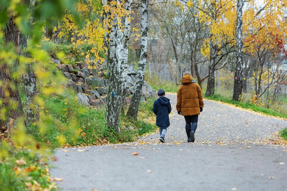 Nainen ja poika kävelevät poispäin kamerasta. On syksyinen sää.