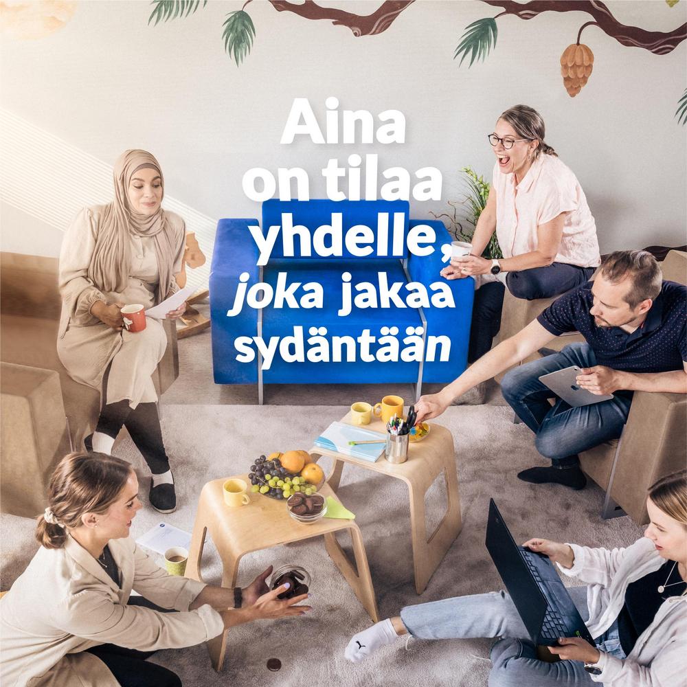 Aina on tilaa yhdelle, joka jakaa sydäntään. Aikuiset istuvat sohvaryhmässä, jonka yksi nojatuoli on tyhjä. Yhdellä henkilöllä on läppäri. Sohvapöydällä on muistiinpanovälineitä sekä kulhossa viinirypäleitä ja keksejä. Henkilöillä on juomamukit kädessä ja he hymyilevät iloisesti.