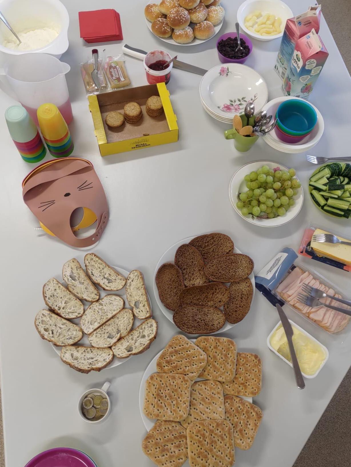 Perhekahvilan aamiaiskattaus: voileipätarvikkeita, jogurttia, maissinaksuja ja laskiaispullia.