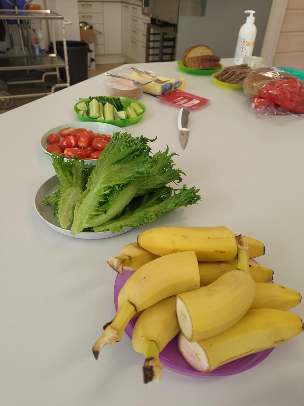 Kuvassa on aamupalatarvikkeita: leipää, margariinia, juustoa, kinkkua, kurkkua, tomaattia, salaattia ja banaaneja.