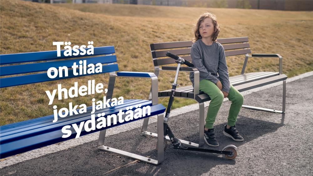 Kaksi penkkiä, joista toinen on tyhjä. Toisella penkillä istuu yksin poika. Tyhjän penkin päällä on teksti: Aina on tilaa yhdelle, joka jakaa sydäntään.