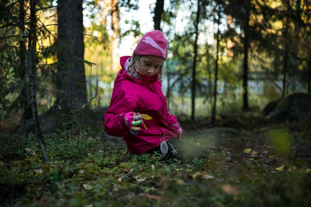 Tyttö polvillaan pinkeissä ulkovaatteissaan metsässä tutkien luontoa.