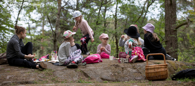 Ohjaajia ja lapsia istuvat metsässä kalliolla ja syövät eväitä. Kuva: Suomen 4H-liitto/Tiina Rinne.