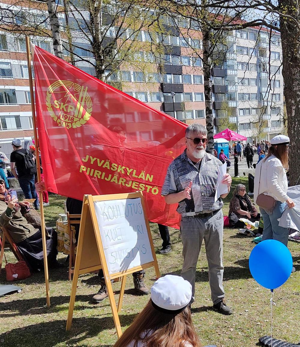 Miguel López pitämässä puhettaan vappuna puistossa. Taustalla SKP Jyväskylän piirin lippu ja Miguelin vieressä kyltti jossa lukee "koulutus, kulttuuri, sivistys".