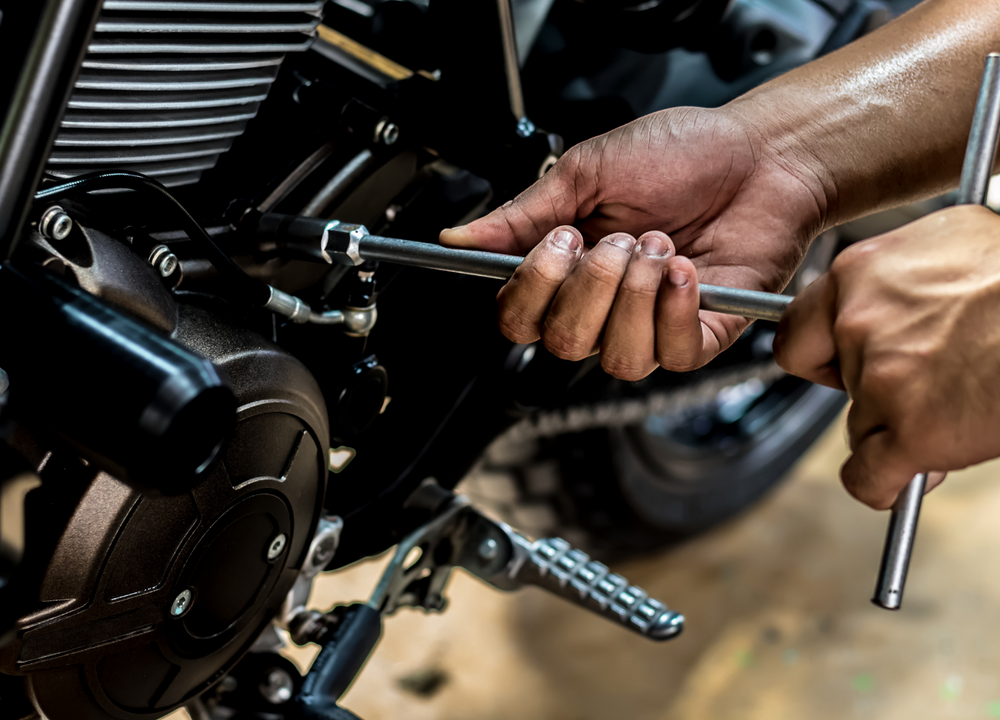 Mopopaja. Miehen kädet korjaamassa moottoripyörää.