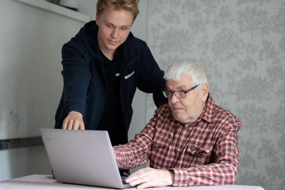 Nuori auttaa vanhusta tietokoneen käytössä.
