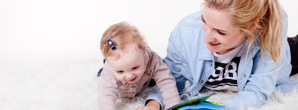 Vanhempi ja pieni lapsi makoilemassa matolla ja lukemassa kirjaa. 