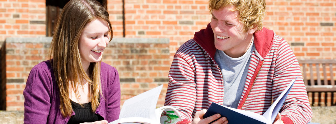 Kaksi nuorta istuu ulkona aurinkoisessa säässä ja opiskelevat yhdessä.