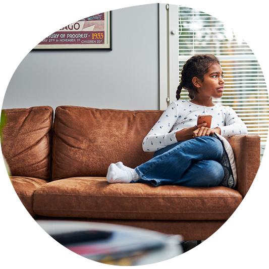 Lapsi istuu sohvolla puhelin kädessä ja katsoo sivullensa kaukaisuuteen.