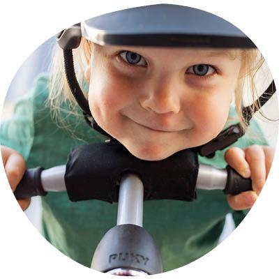 Hymyilevä lapsi kypärä päässä potkulaudan kanssa.