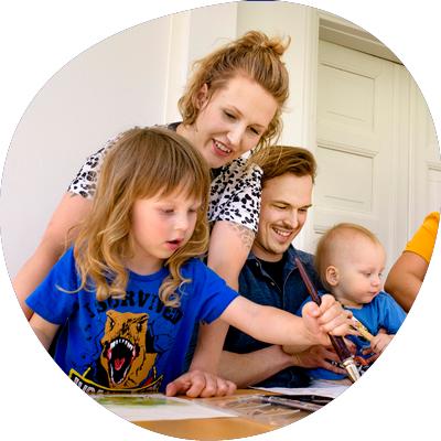 Aikuisia ja lapsia maalamassa pöydän ääressä.