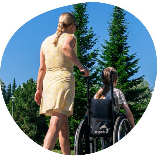 Aikuinen ja lapsi kulkevat ulkona, lapsi on pyörätuolissa ja henkilöt näkyvät takaapäin.