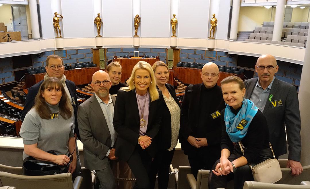 Ryhmäkuvassa kansanedustaja Pia Kauma ja tapaamiseen osallistuneet kahdeksan yhdistyksen jäsentä täysistuntosalin lehtereillä