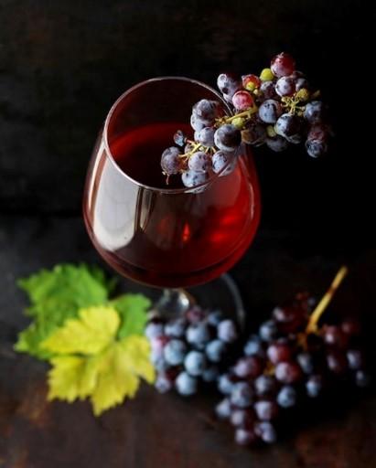 Punaviiniä lasissa, ympärillä tummia viinirypäleitä.
