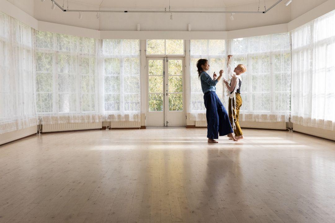 Kaksi naista tanssimassa vaaleassa salissa jossa on reunoilla ikkunoita.