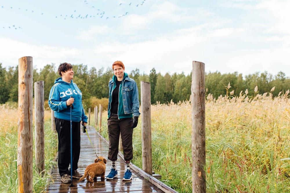 Kaksi henkilöä ja koira esteettömällä luontopolulla.