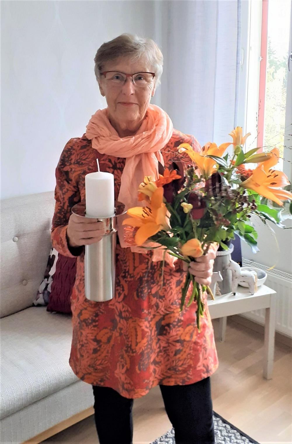 Muistilähettiläs Seija Helminen kukkien ja muistilähettilään kynttilänjalan kanssa.