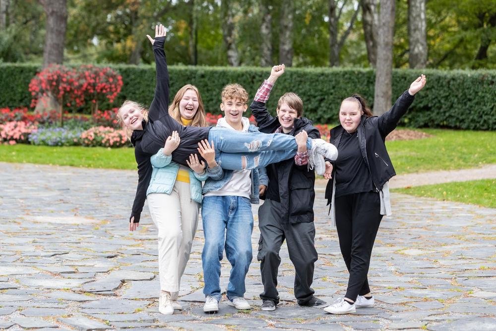 Valokuva: Puistokivetyksellä seisoo joukko iloisia ja käsiään heiluttelevia nuoria, jotka kannattelevat yhdessä syleissään poikittain yhtä nuorista.