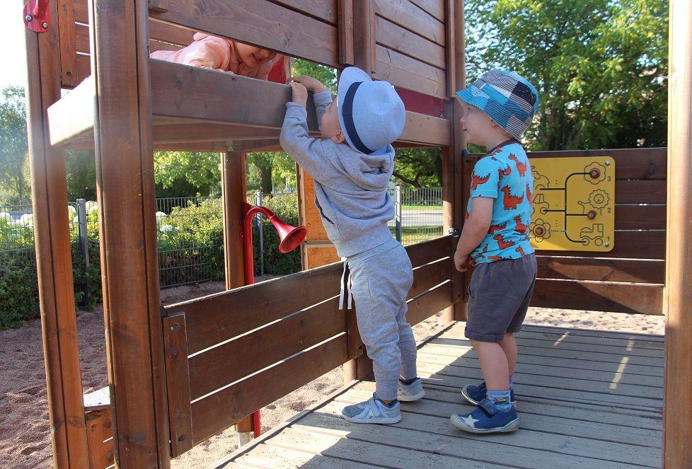 Valokuva: Kesäisessä kuvassa on leikkipuiston teline, jonka päälle on kiivennyt kaksi lasta. 