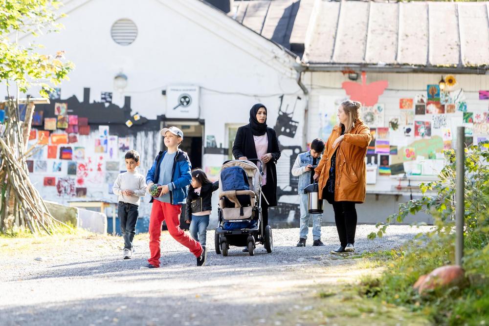Valokuva: Ulkona kävelemässä kaksi naista ja heidän lapsensa. Toinen heistä työntää lastenvaunuja ja on pukeutunut hijabiin. Lapset kulkevat naisten lähellä.