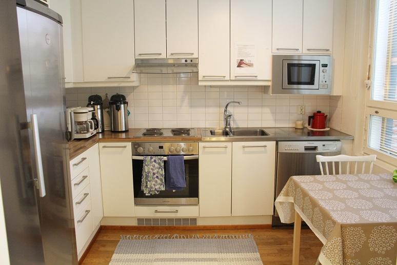 Valokuva: Kuvassa Laivapuiston perhetalon keittiö. Tilassa näkyy pakastin ja jääkaappi, laskutasot, uuni/liesi, mikroaaltouuni ja apupöytä.