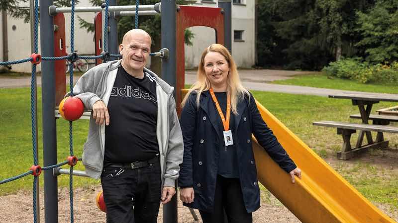 Emmi Vaalasmaa ja Oskari Perholehto seisovat hymyillen taloyhtiön leikkipuiston kiipeilytelineen ja liukumäen edessä. 
