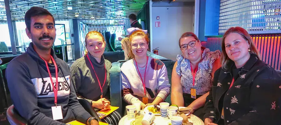 Aayuh Jain, Noora Suomalainen, Eveliina Weidenbacher, Riikka Pasanen ja Niina Lindström istumassa pienen pyöreän pöydän äärelä risteilylaivan tiloissa.