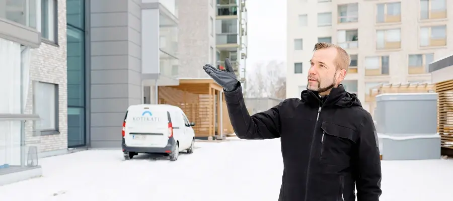 Tomi Henriksson seisomassa lumisella kerrostalon pihalla mustassa talvitakissa. Hän viittaa kädellään vieressä olevaan taloon. 