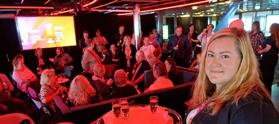 Maria Aspala hymyilee taustallaan ryhmä ihmisiä laivan kokoustiloissa.