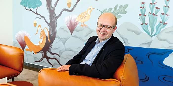 MLL:n johtava asiantuntija Esa Iivonen istumassa hymyillen oranssilla sohvatuolilla.