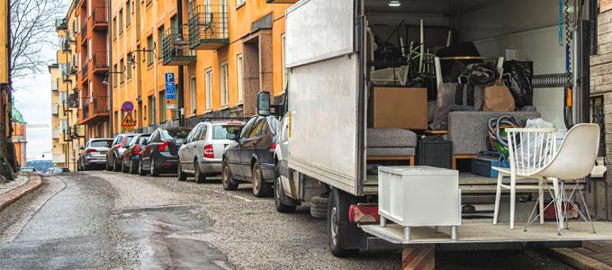 Ett antal bilar står parkerade på sidan av gatan. En av dem är en flyttbil som rör sig med rörliga lådor och möbler.