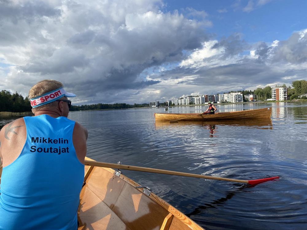 Kaksi soutajaa soutamassa puuvenettä järvellä. 