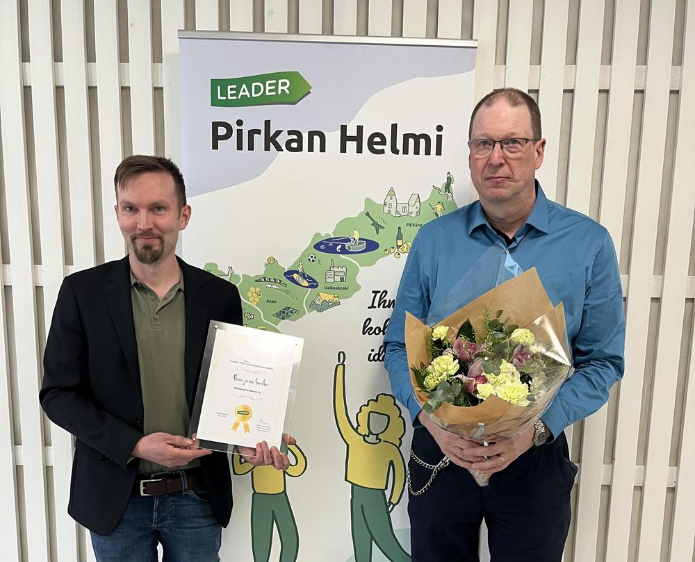 Kuvassa poseeraavat Simo Tuominen kunniakirjan ja Janne Jamalainen kukkakimpun kanssa. 