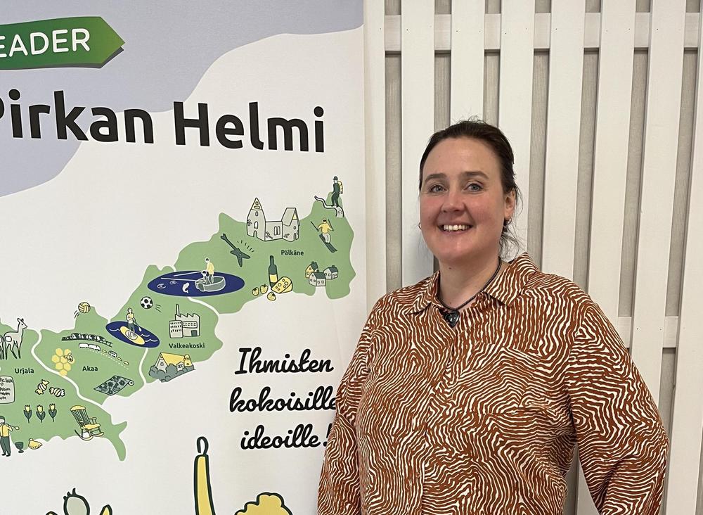 Kuvassa Sari Junnila poseeraan Pirkan Helmen rollupin edessä hymyillen.