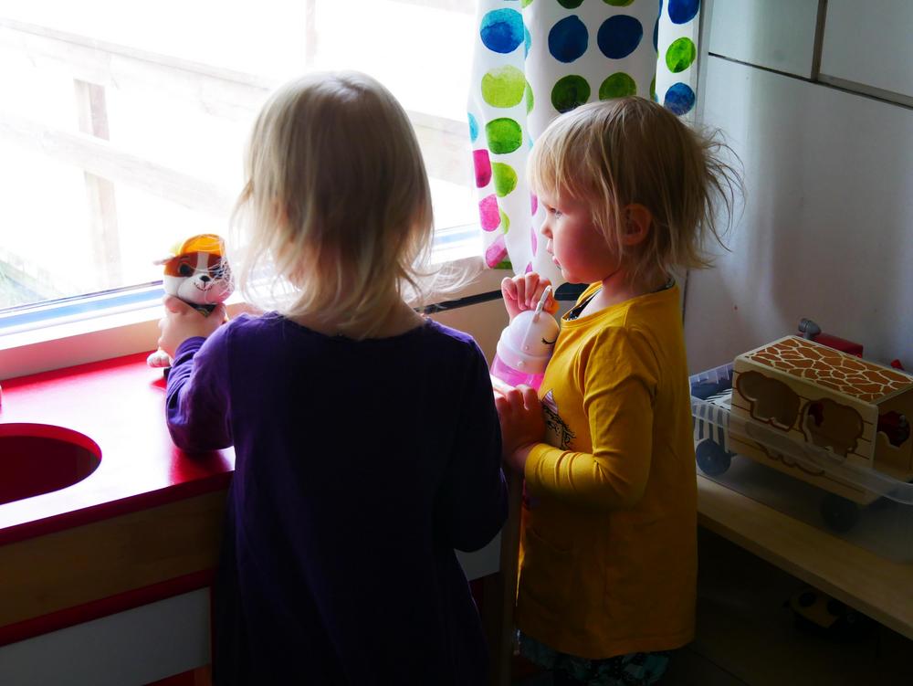 Kaksi pientä tyttöä leikkii ikkunan ääressä.