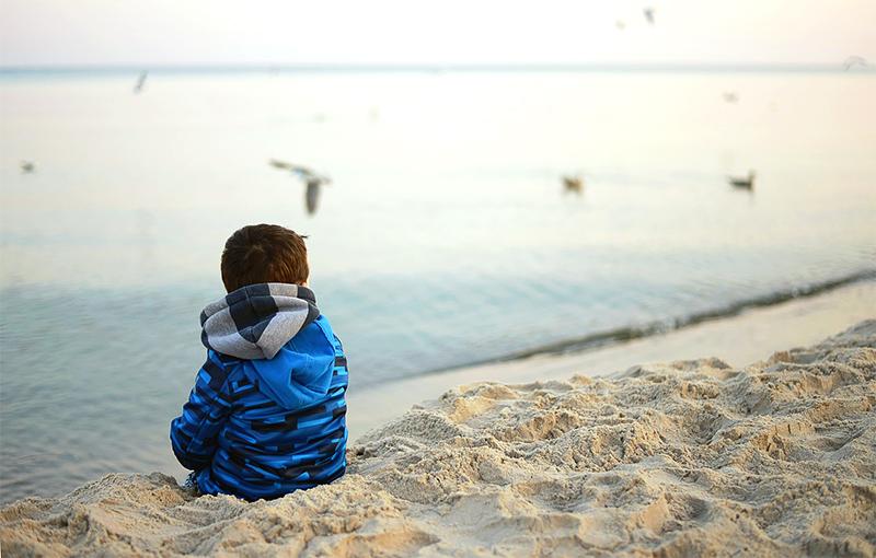 Pieni poika istuu rannalla.