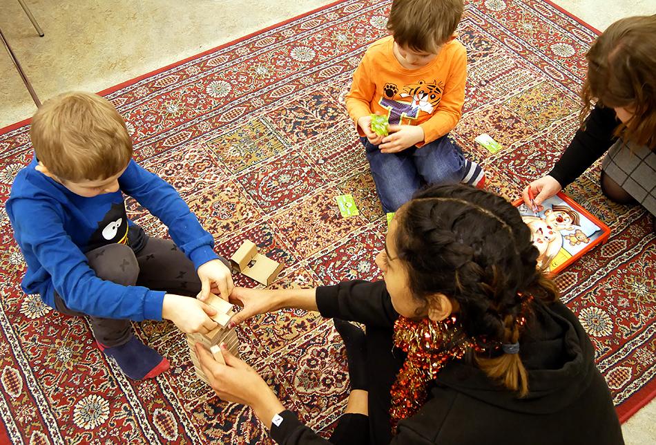 Kolme lasta ja lastenhoitaja leikkivät lattialla.