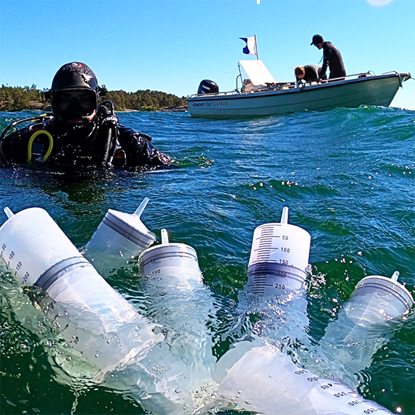Syringes in water, a diver an a boat in the background