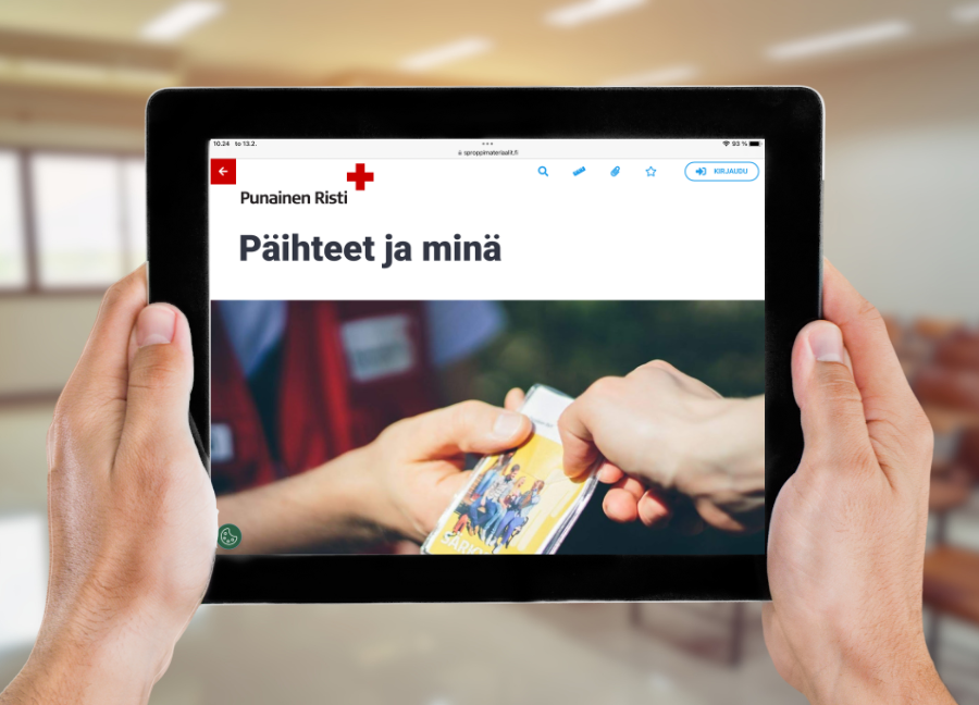 Käsissä tabletti, jonka näytöllä on auki Punaisen Ristin Päihteet ja minä -opetusmateriaali. Taustalla näkyy luokkahuone.