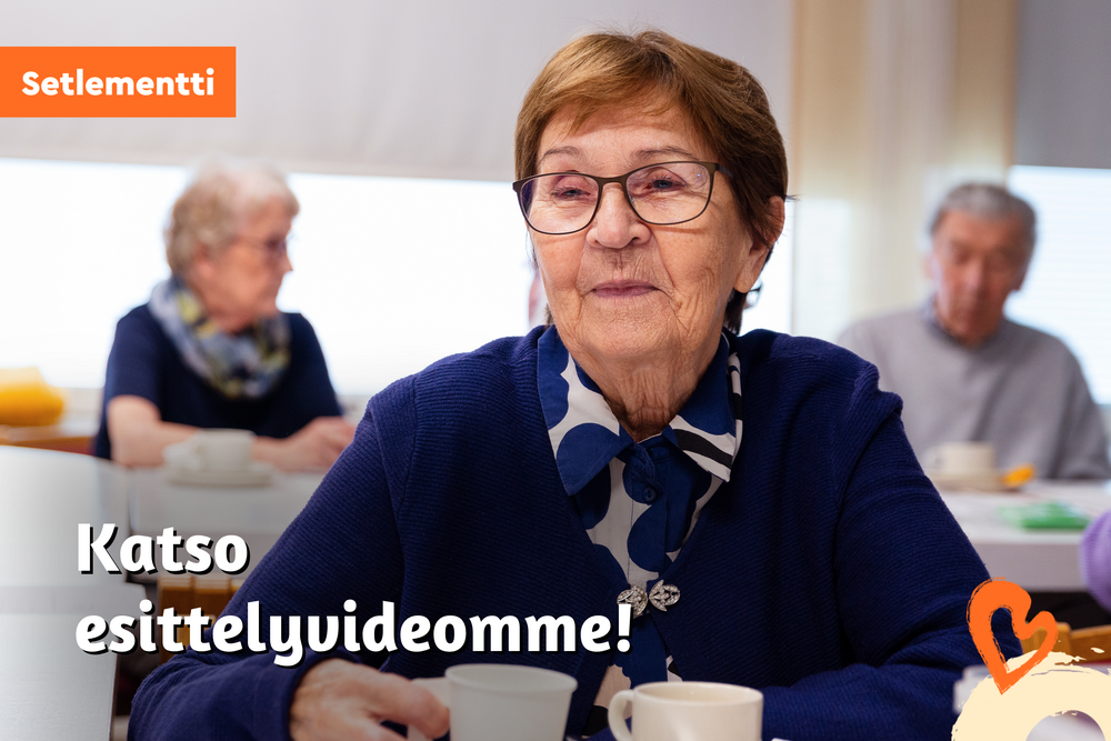 Hymyilevä vanhus istuu pöydässä kahvikupin kanssa.