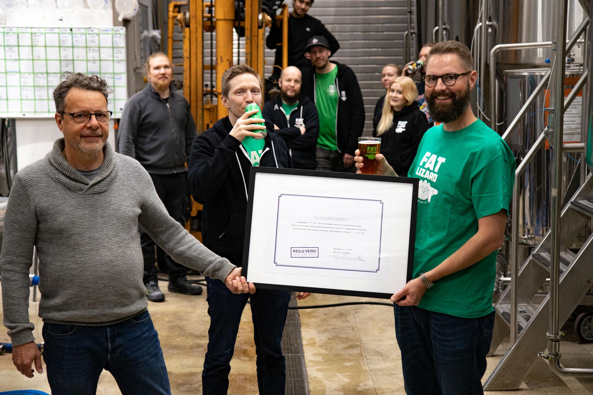 Kuvassa Reilu vero ry:n puheenjohtaja Kim Remitz luovuttaa Reilu vero -sertifikaatin Fat Lizard Brewing Companyn edustajille panimon tiloissa Espoossa.