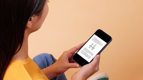 Henkilö pitelee kädessään puhelinta, jossa on tekstiä ja kuva kahdesta hahmosta.